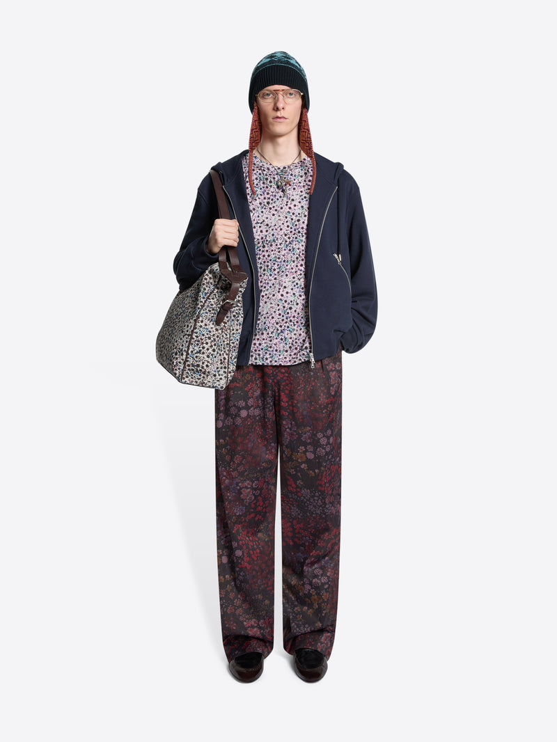 Person wearing a dark hoodie, patterned pants, and a beanie holding a bag on a white background