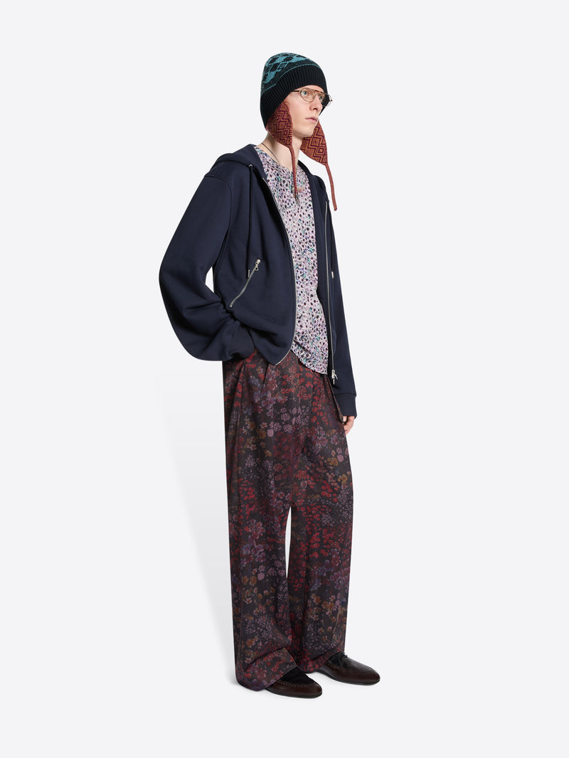 Person wearing a dark hoodie, patterned pants, and a beanie