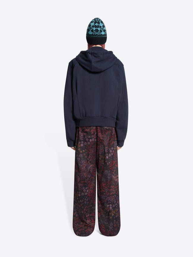Person wearing a dark hoodie and patterned pants with a beanie on a white background