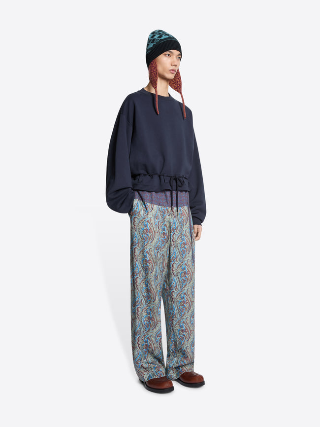 Person wearing a navy sweatshirt and patterned pants on a white background