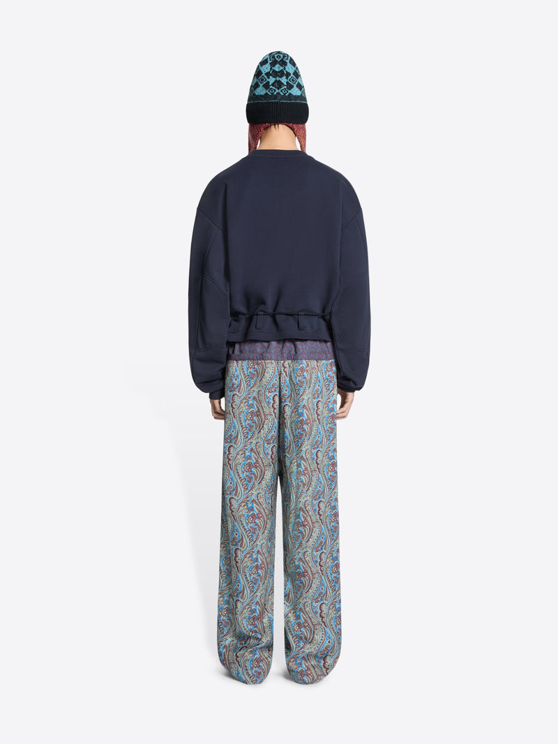 Person wearing a navy sweatshirt and patterned pants on a white background