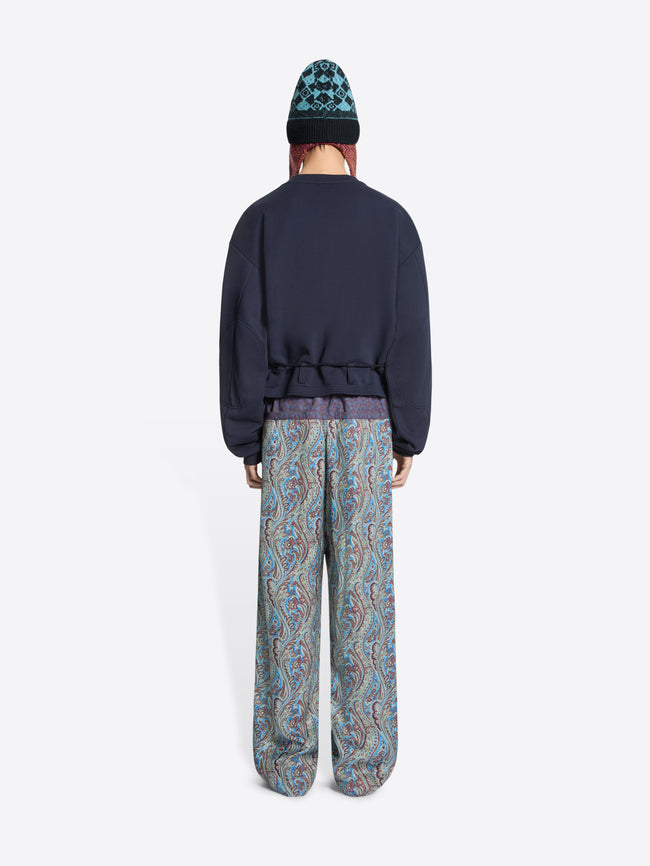 Person wearing a navy sweatshirt and patterned pants on a white background