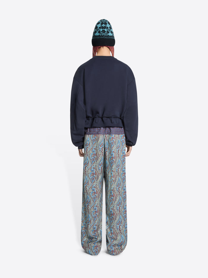 Person wearing a navy sweatshirt and patterned pants on a white background