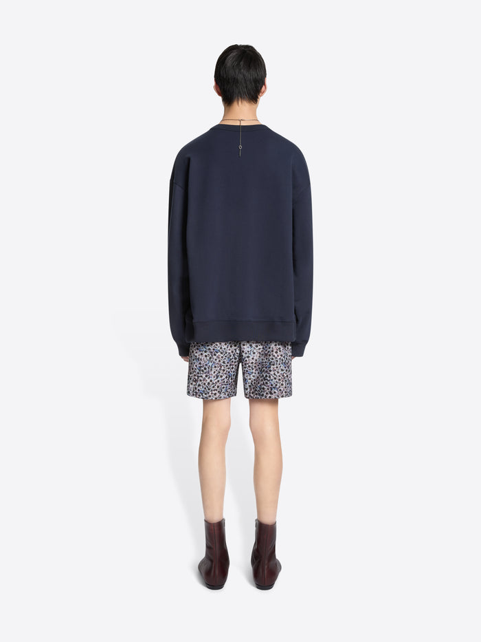 Person wearing a navy sweater and patterned shorts on a white background