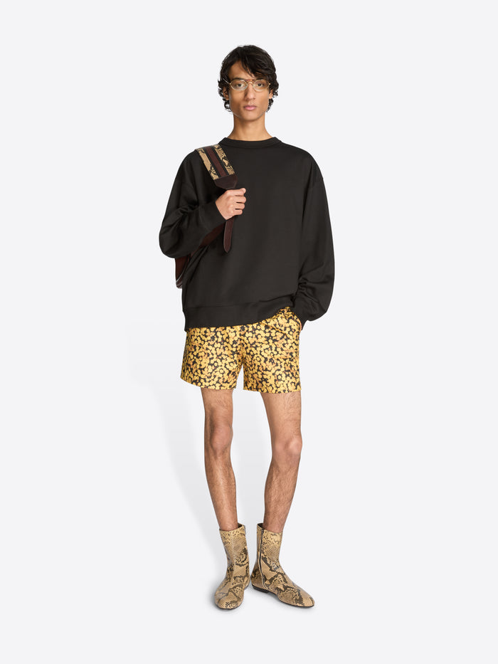Person wearing a black sweatshirt, patterned shorts, and snake print boots on a white background