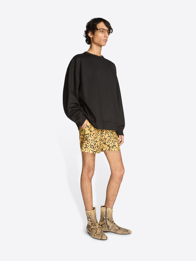 Person wearing a black sweatshirt, patterned shorts, and snake print boots on a white background