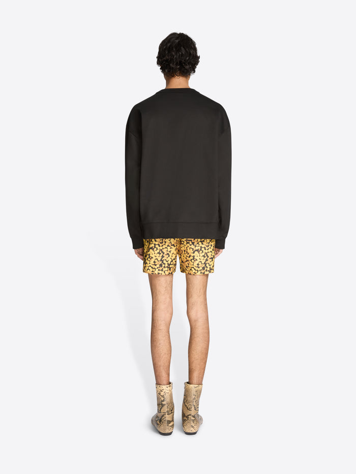 Person wearing a black sweater and patterned shorts on a white background