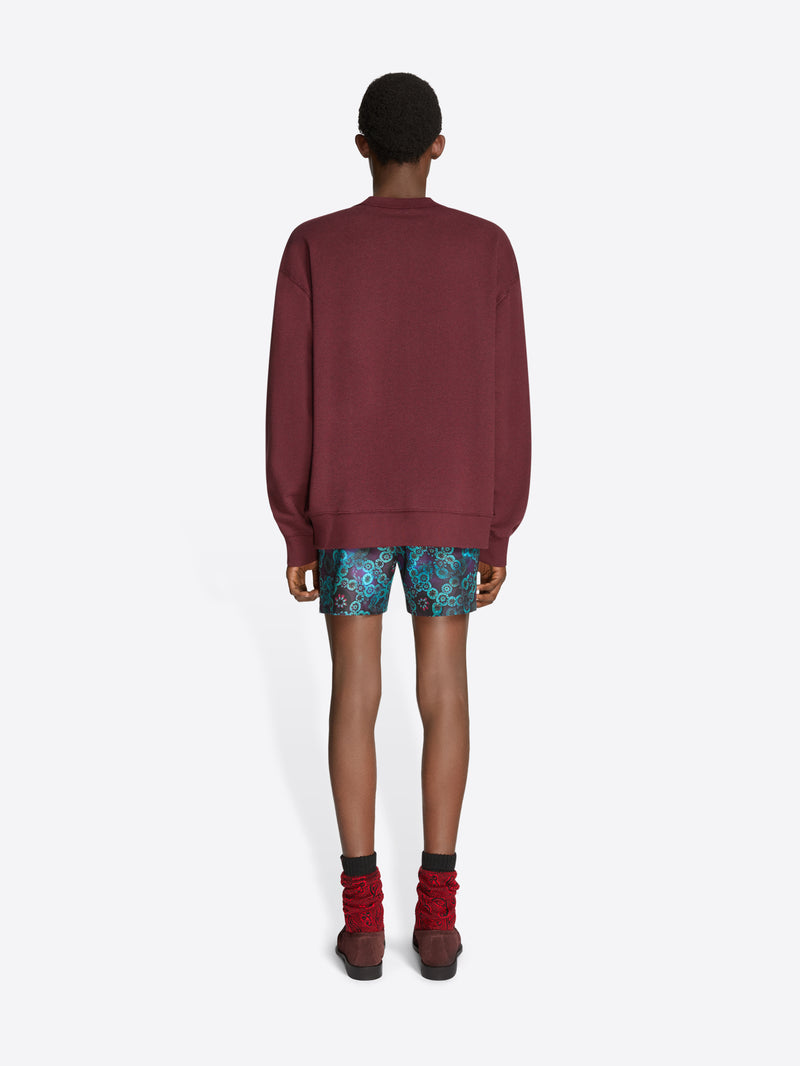 Person wearing a burgundy sweatshirt, patterned shorts, and brown shoes on a white background