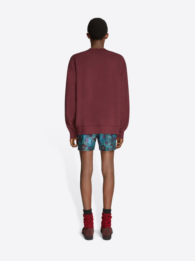Person wearing a burgundy sweatshirt, patterned shorts, and brown shoes on a white background