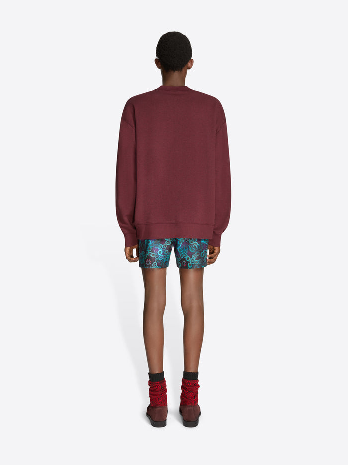 Person wearing a burgundy sweatshirt, patterned shorts, and brown shoes on a white background