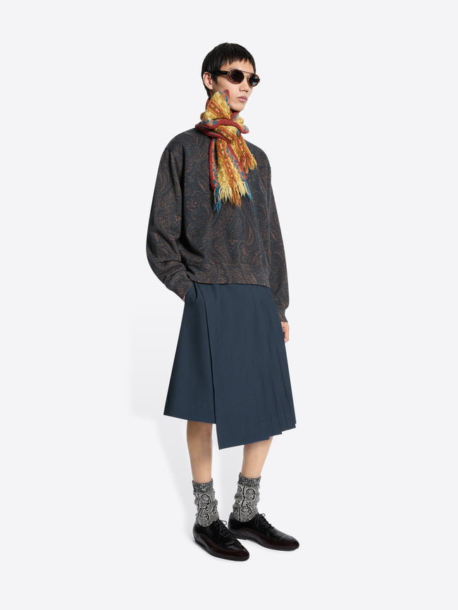 Person wearing a patterned sweatshirt, dark skirt, and colorful scarf on a white background