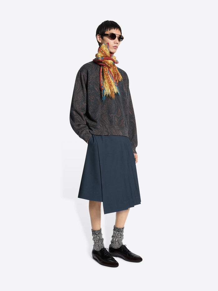 Person wearing a patterned sweatshirt, dark skirt, and colorful scarf on a white background