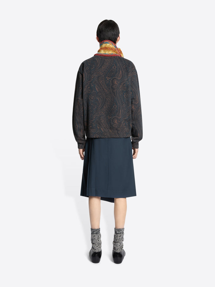 Back view of a person wearing a patterned sweatshirt, dark skirt, and colorful scarf on a white background