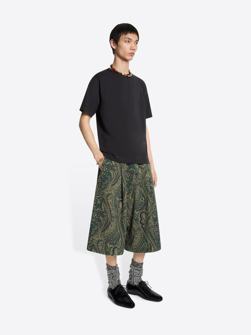 Person wearing a black t-shirt and green patterned pants on a white background