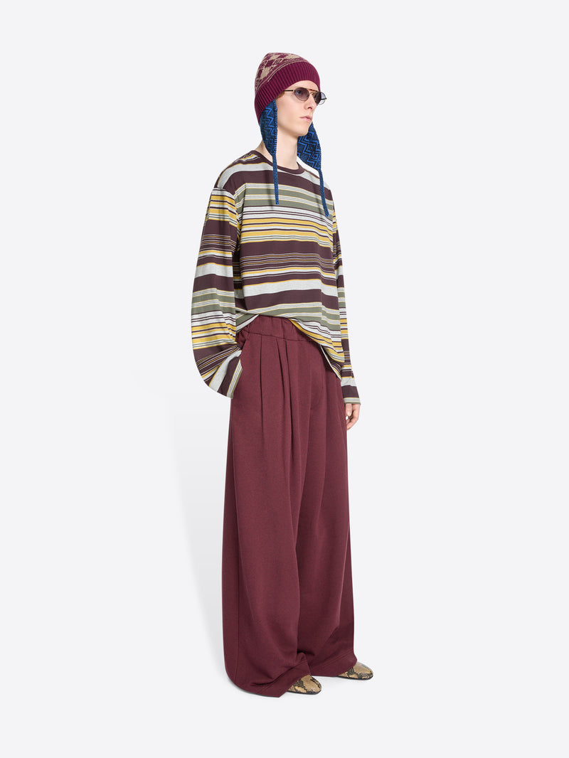 Person wearing a striped long-sleeve, wide-leg pants and a patterned hat on a white background