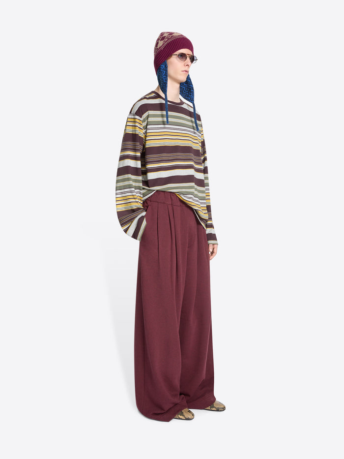 Person wearing a striped long-sleeve, wide-leg pants and a patterned hat on a white background
