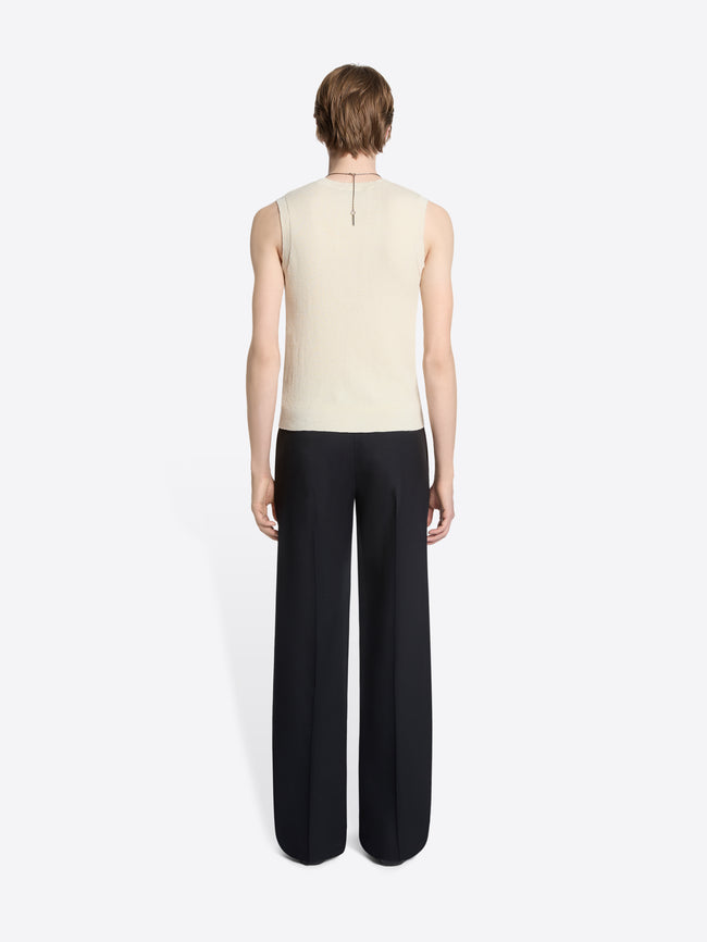 Back view of a person wearing a sleeveless patterned knitted top and black pants on a white background
