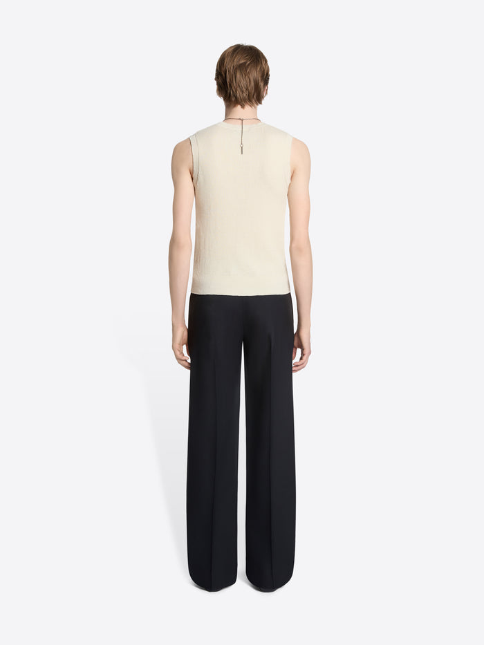 Back view of a person wearing a sleeveless patterned knitted top and black pants on a white background