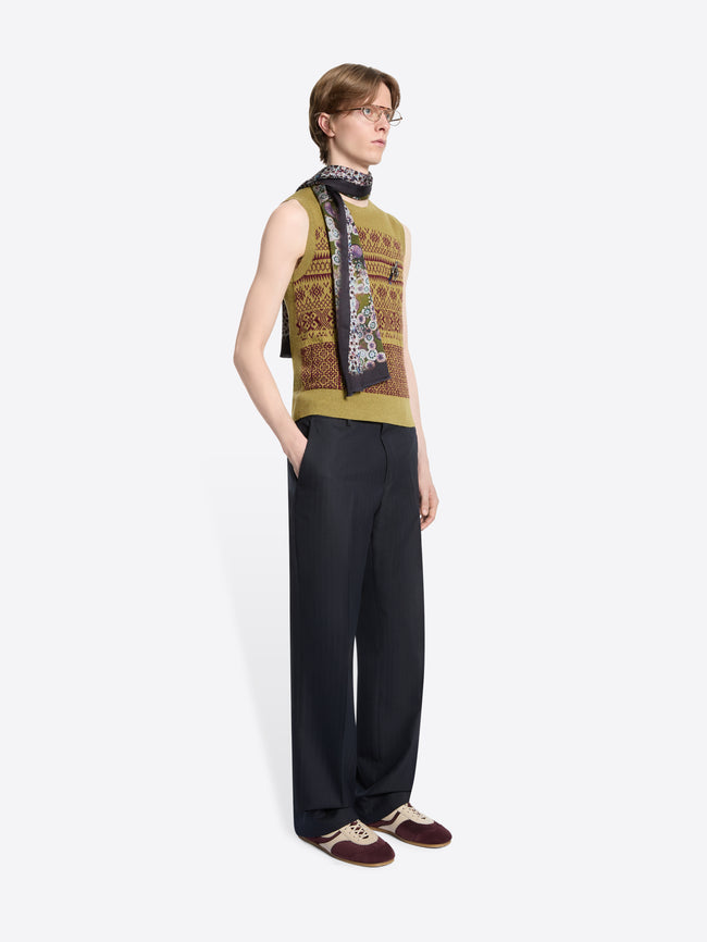 Person wearing a patterned sleeveless top and dark pants on a white background