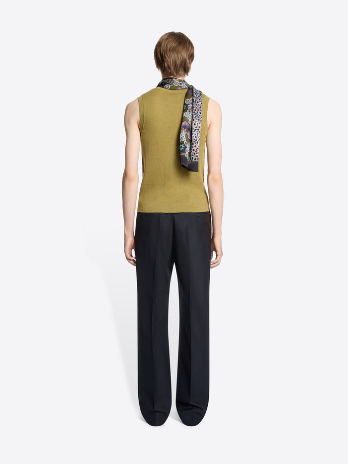 Back view of a person wearing a green sleeveless top and black pants with a patterned scarf over their shoulder on a white background
