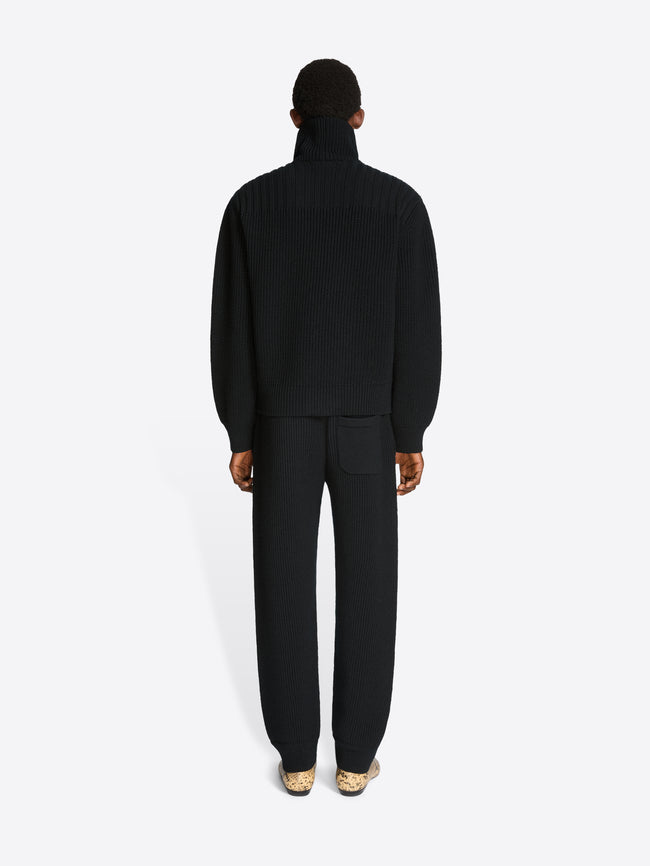 Back view of a man wearing a black ribbed knit cardigan and matching pants with a white background