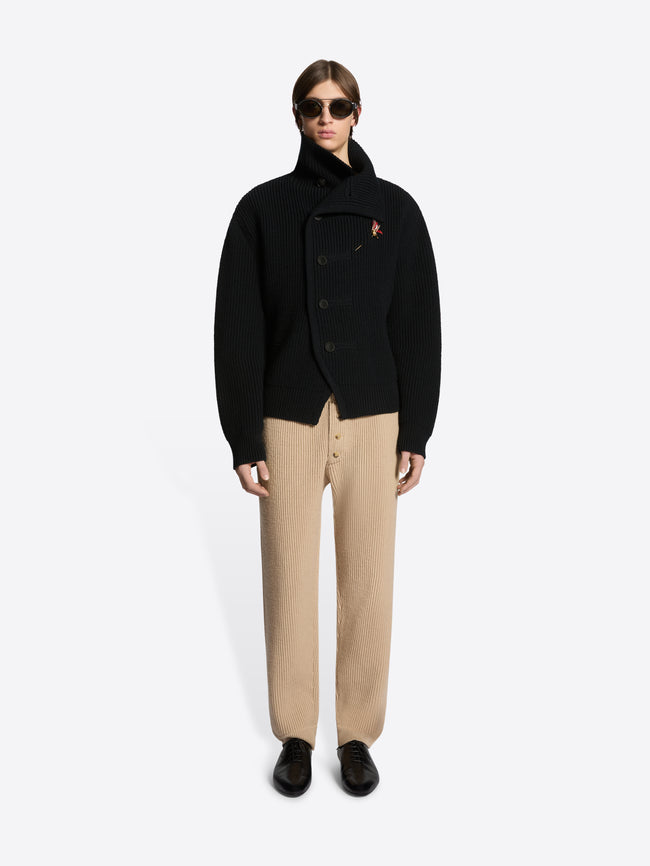 Person wearing a black coat logo and beige pants on a white background