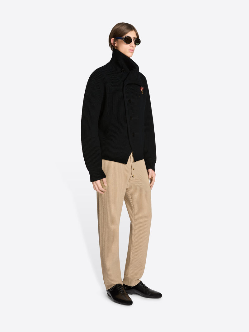 Person wearing a black coat and beige pants on a white background