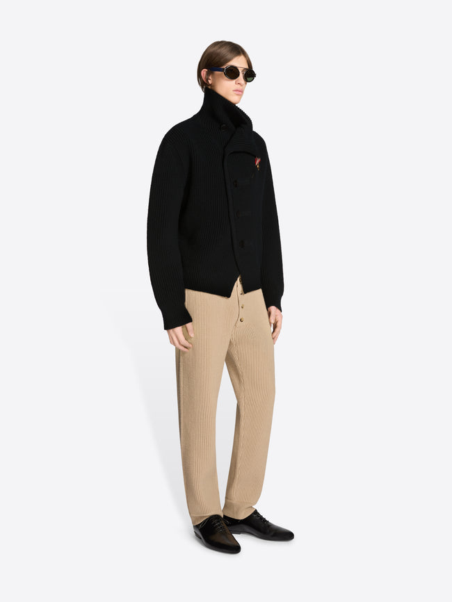 Person wearing a black coat and beige pants on a white background