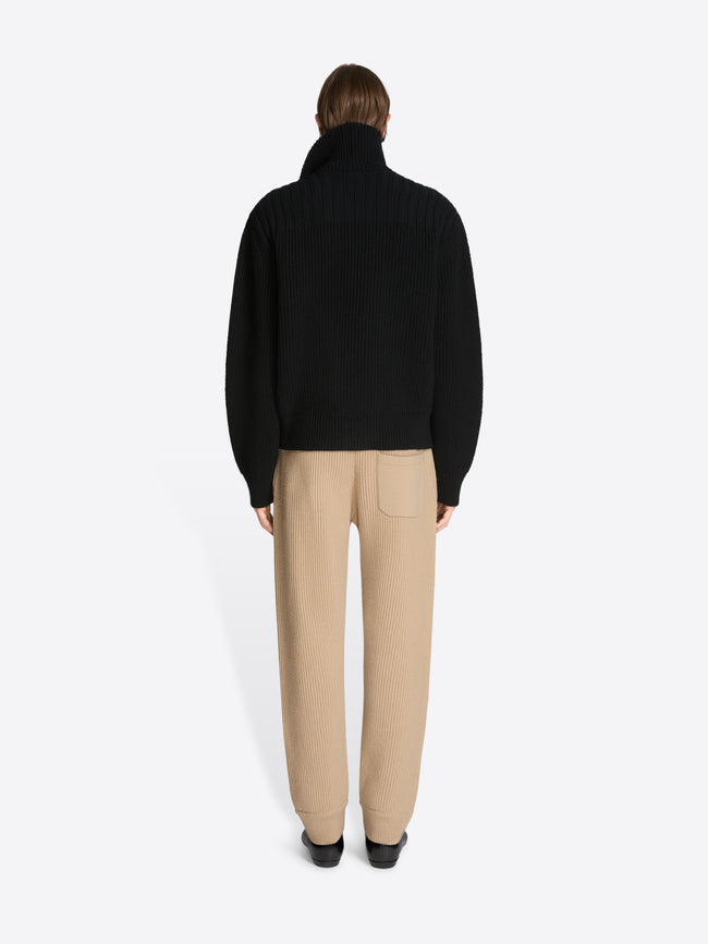 Back view of a person wearing a black coat and beige pants on a white background