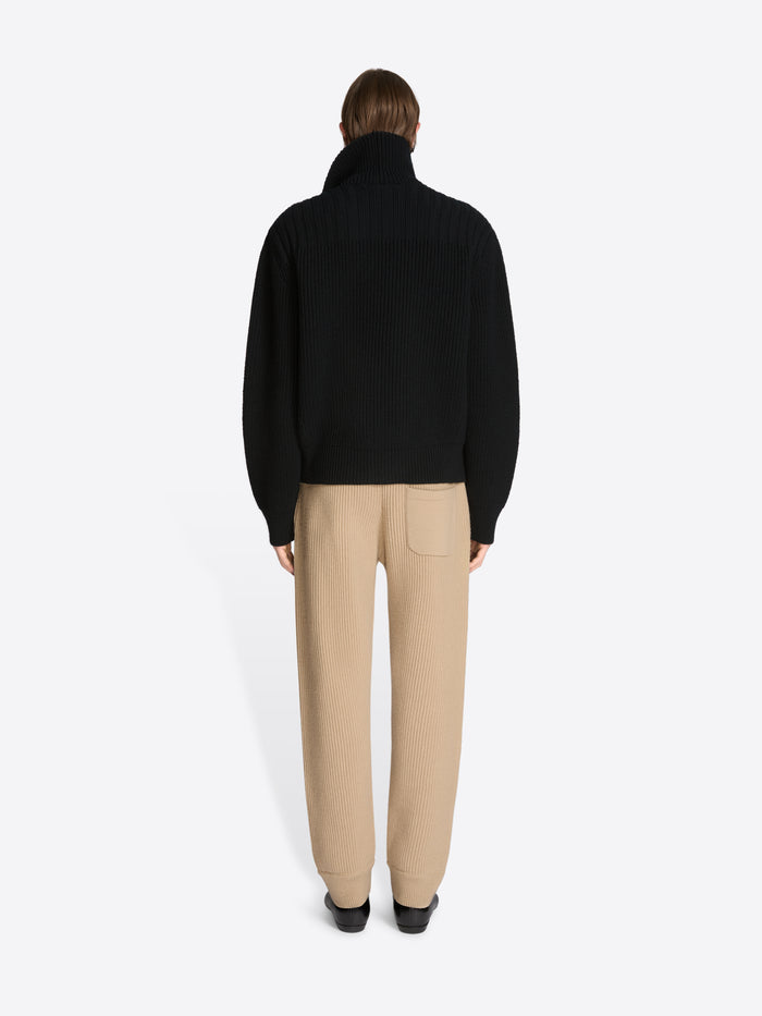 Back view of a person wearing a black coat and beige pants on a white background