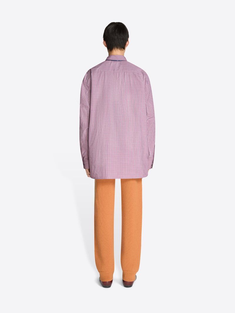 Back view of a person wearing a checkered purple shirt, orange pants, and brown shoes on a white background