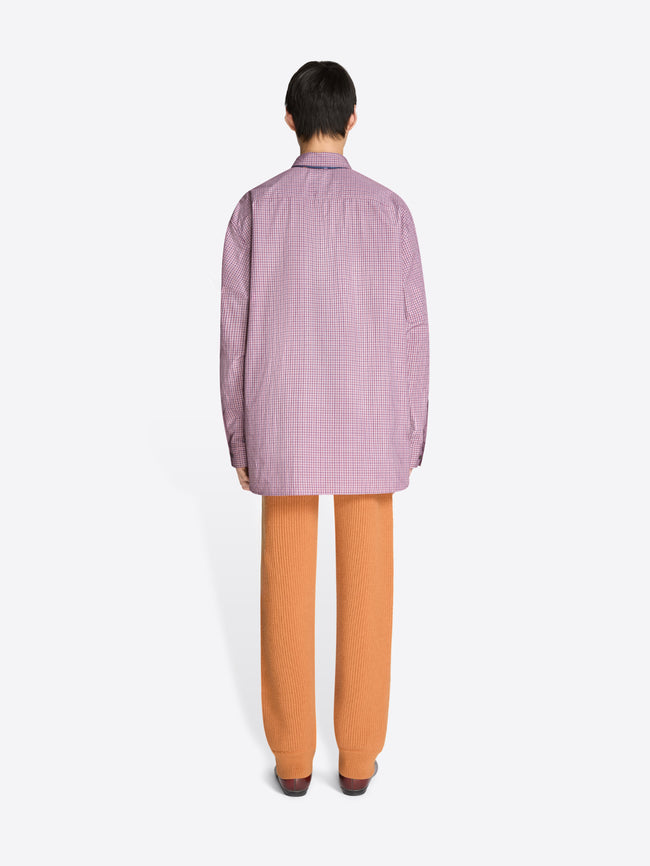 Back view of a person wearing a checkered purple shirt, orange pants, and brown shoes on a white background