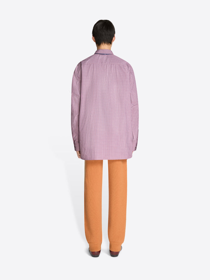 Back view of a person wearing a checkered purple shirt, orange pants, and brown shoes on a white background