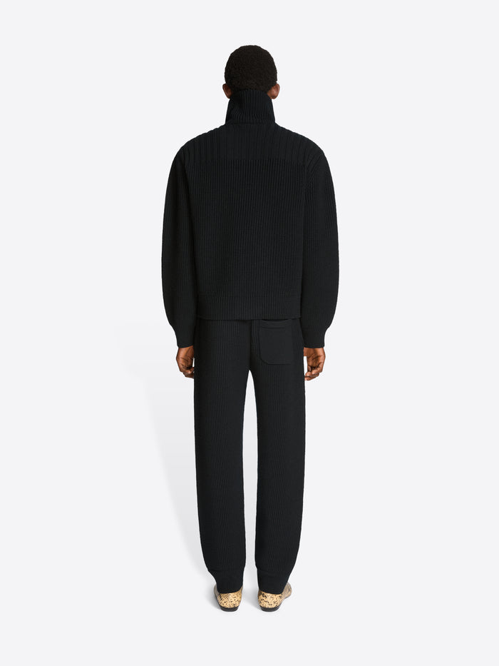 Back view of a person wearing a black set with coat and pants on a white background 