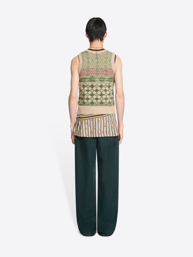 Back view of a person wearing a patterned sleeveless top and dark pants on a white background