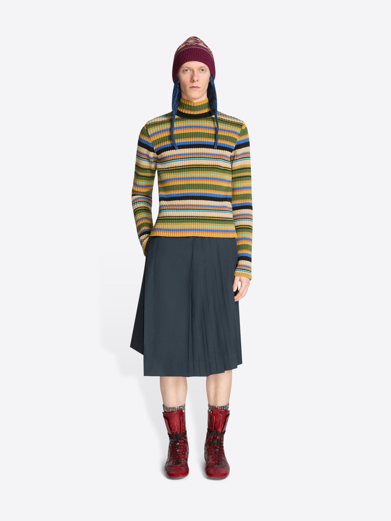 Person wearing a colorful striped sweater, dark skirt, patterned hat and red boots on a white background