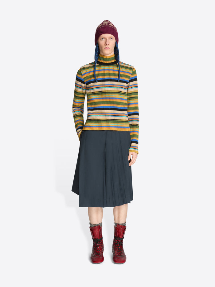 Person wearing a colorful striped sweater, dark skirt, patterned hat and red boots on a white background