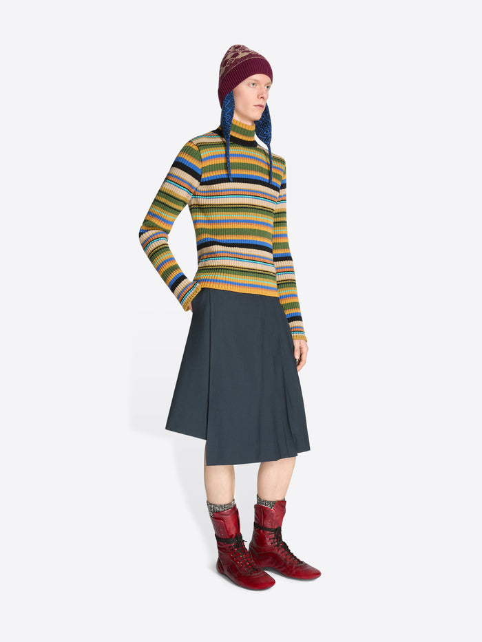 Person wearing a colorful striped sweater, dark skirt, patterned hat and red boots on a white background