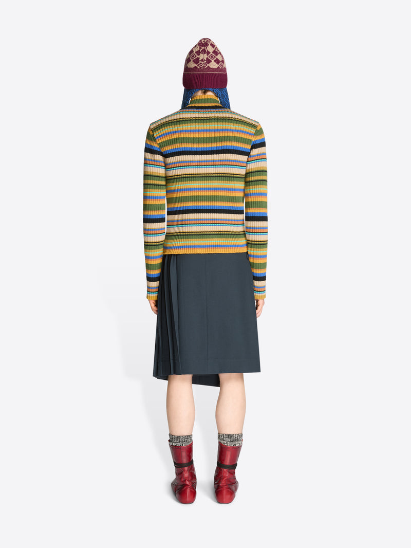 Back view of a person wearing a colorful striped sweater, dark skirt, patterned hat and red boots on a white background