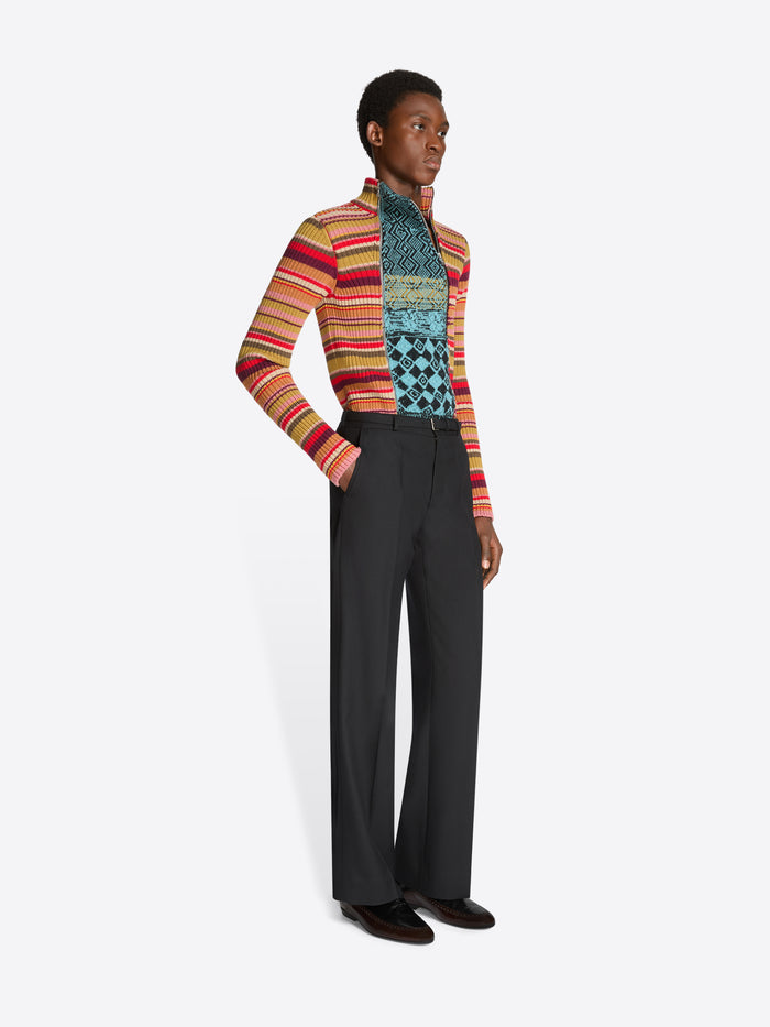 Person wearing a colorful patterned sweater and black pants on a white background