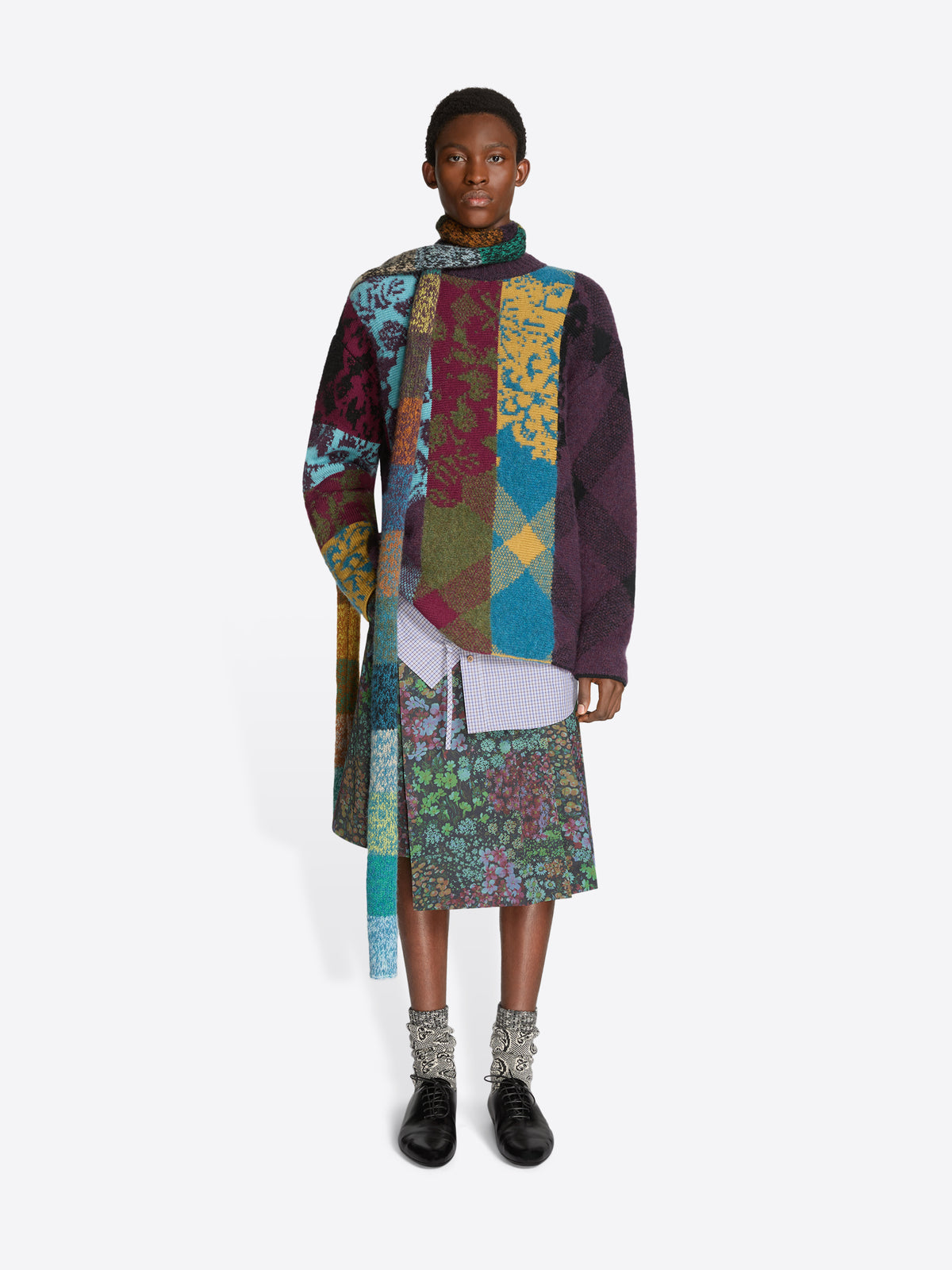 Person wearing a colorful patchwork sweater and floral patterned skirt on a white background