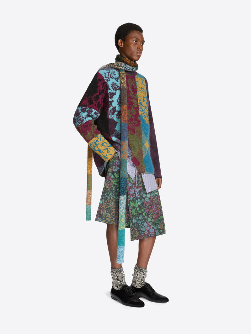 Person wearing a colorful patchwork sweater and floral patterned skirt on a white background