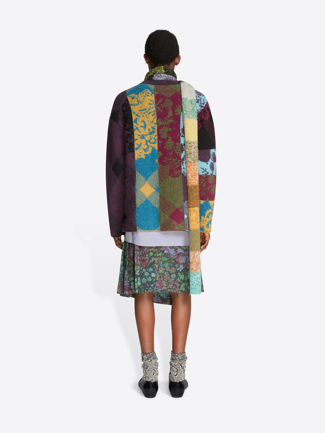 Back view of a person wearing a colorful patchwork sweater and floral patterned skirt on a white background