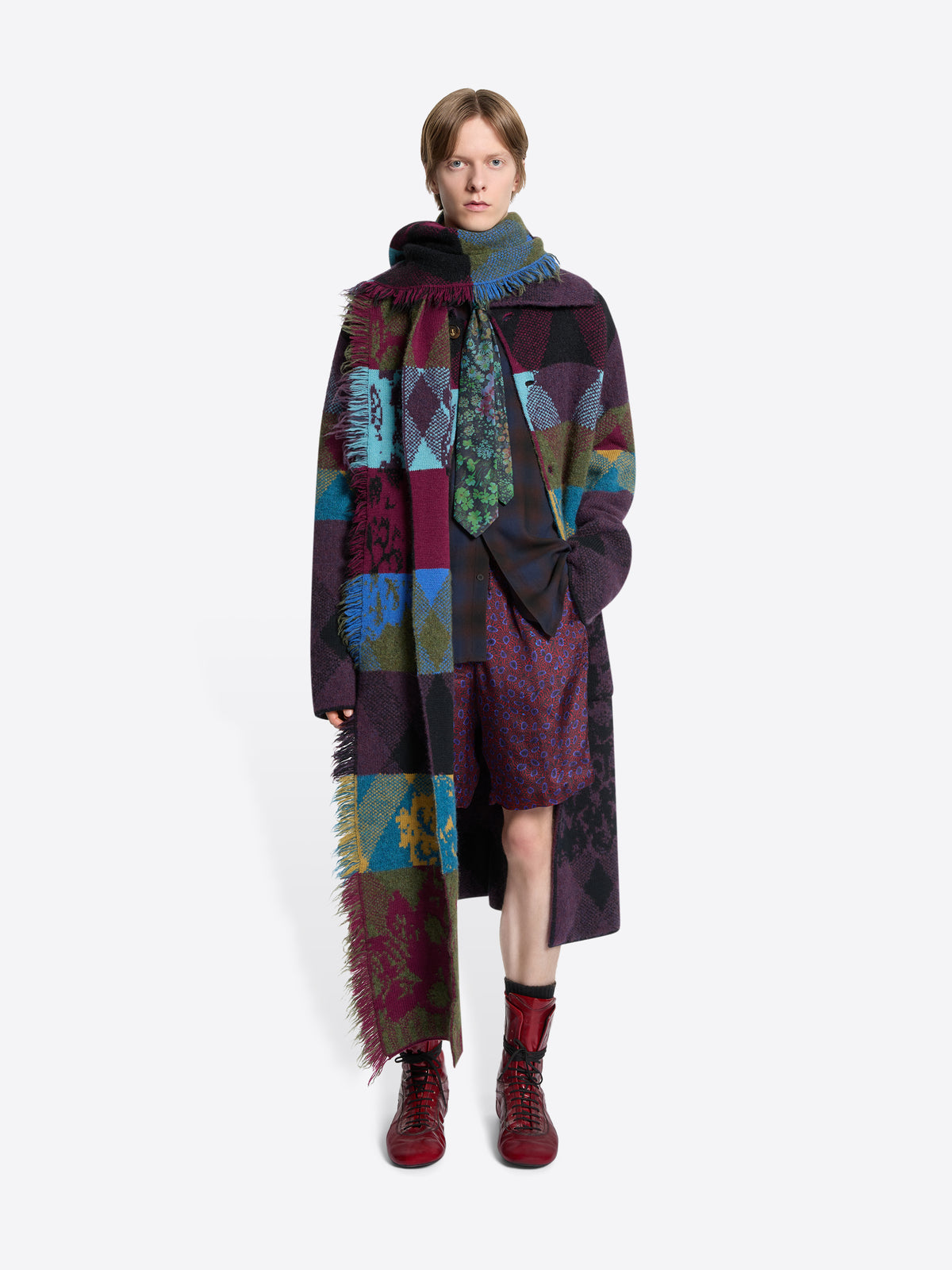 Person wearing a colorful patchwork coat with a scarf on a white background