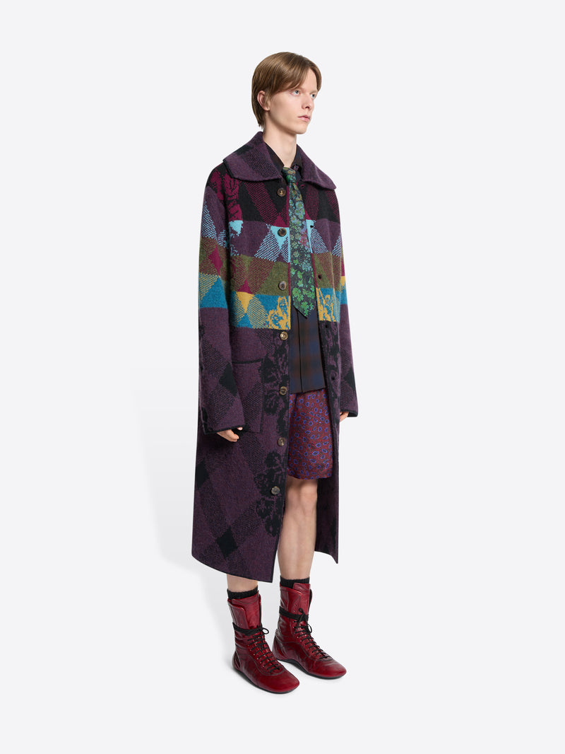 Person wearing a long, patterned coat with a colorful design on a white background
