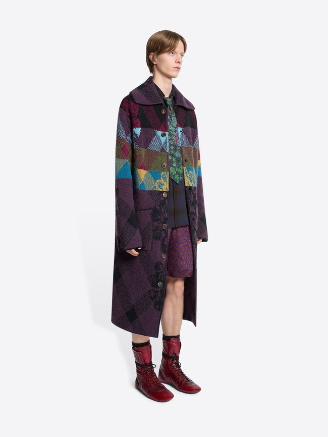 Person wearing a long, patterned coat with a colorful design on a white background