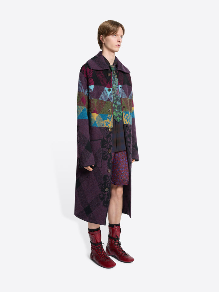 Person wearing a long, patterned coat with a colorful design on a white background