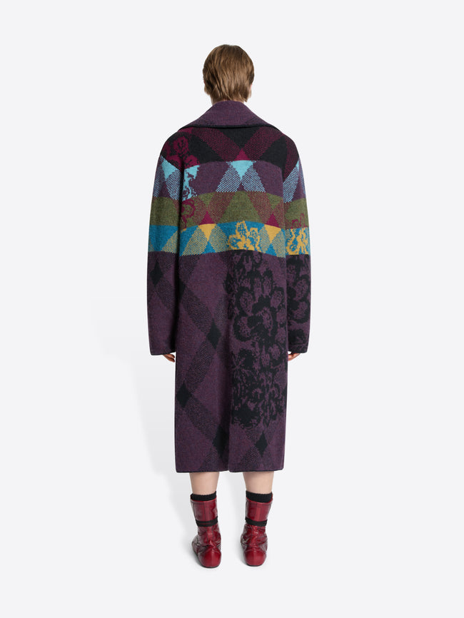 Back view of a person wearing a long, patterned coat with a colorful geometric design on a white background
