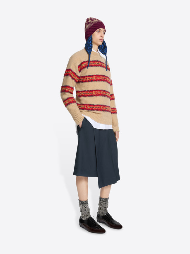 Person wearing a striped sweater, skirt, and patterned hat on a white background