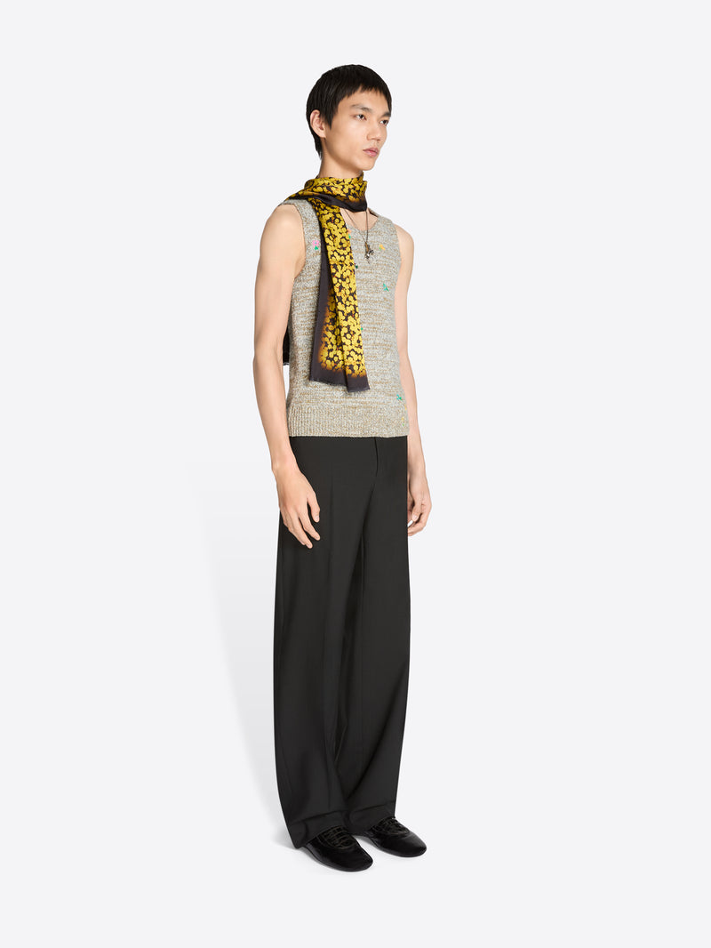 Person wearing a sleeveless top with a patterned scarf and black pants on a white background